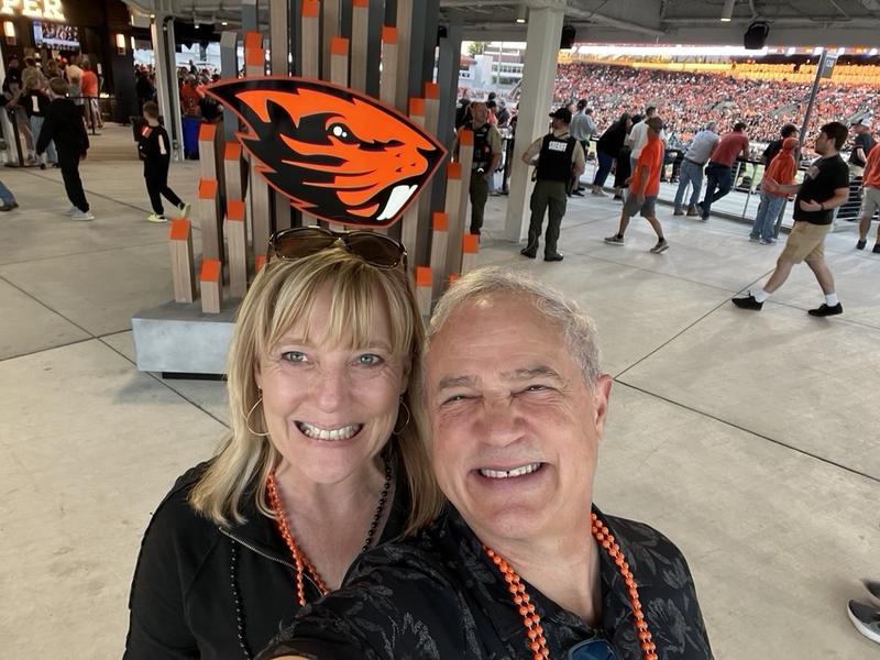 Mark and Lisa Marie Boyd in orange beads at an Oregon State Beavers football game, with the Beavers logo behind them