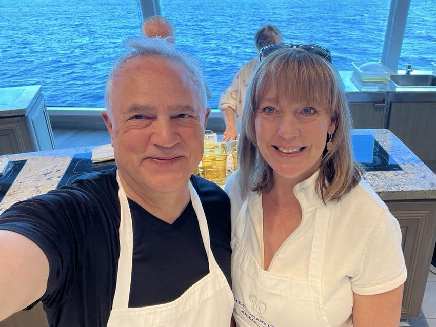 Mark and Lisa Marie Boyd in aprons at a cruise-ship cooking class with an ocean view behind them