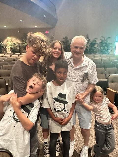 Mark Boyd in a white patterned shirt with five of his grandkids goofing around in an auditorium