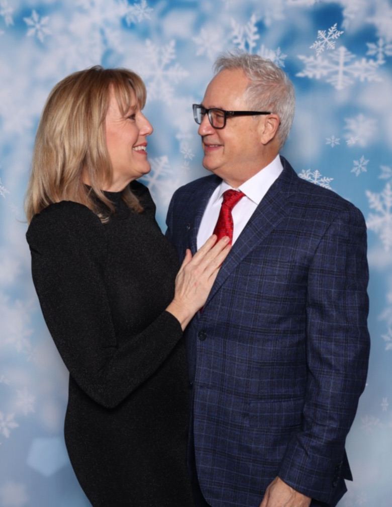 Mark Boyd in a navy plaid blazer and red tie with Lisa Marie against a snowflake backdrop, looking at each other