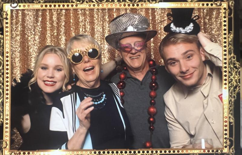 Mark Boyd in a sequined hat and novelty glasses with family in a photo booth